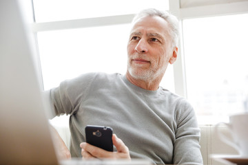 Photo of focused mature man working with laptop and cellphone