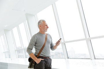 Photo of handsome gray-haired man typing on cellphone while standing