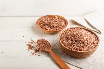 Two wooden bowls with unpolished brown rice and wooden spoon on a white wooden background. Side view, copy space.