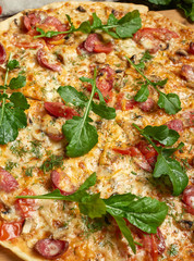 baked round pizza with smoked sausages, mushrooms, tomatoes, cheese and arugula leaves