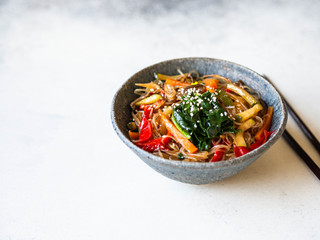 Blue bowl with rice noodles and various vegetables steer fry on a grey background.