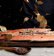 headless salmon filet on a wooden board sprinkled with leaves of dry bay leaves