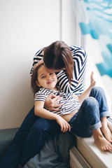 Fototapeta premium Mother and daughter sitting at the window at home hugging and having fun
