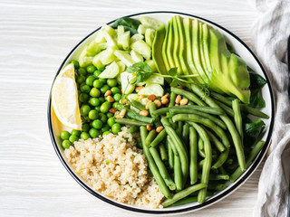 Quinoa bowl with green beans, green peas, cucumber, avocado, and pine nuts on grey background. Copy space