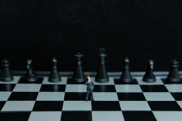 Business strategy conceptual photo - Miniature of businessman thinking in front of chess board