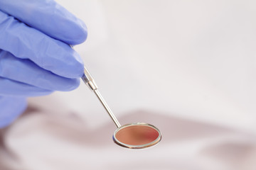 Dentist's hand with mouth mirror in blurred background.