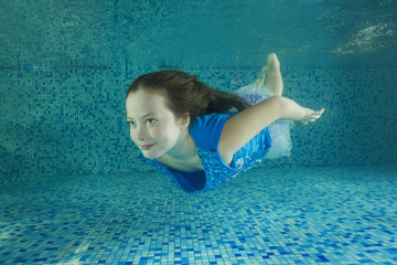 Girl in blue dress swims underwater in the swimming pool.