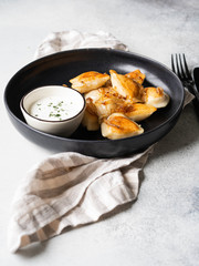 Traditional Polish dish - pierogi or dumplings or vareniki potatoes and mushrooms with sour cream and fried onions in black plate on grey background