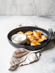 Traditional Polish dish - pierogi or dumplings or vareniki potatoes and mushrooms with sour cream and fried onions in black plate on grey background