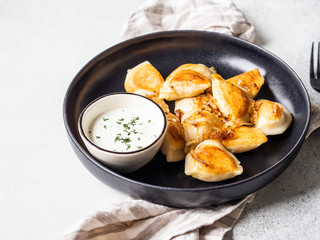 Traditional Polish dish - pierogi or dumplings or vareniki potatoes and mushrooms with sour cream and fried onions in black plate on grey background