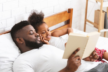 Loving african father reading fairy tales to his small daughter