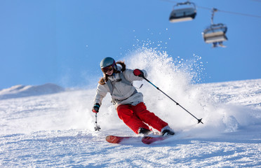 Girl On the Ski. a skier in a bright suit and outfit with long pigtails on her head rides on the track with swirls of fresh snow. Active winter holidays, skiing downhill in sunny day. Woman skier - obrazy, fototapety, plakaty