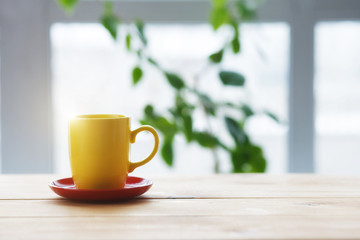 yellow coffee cup on wooden table, blurred nature background, copy space, morning sunlight