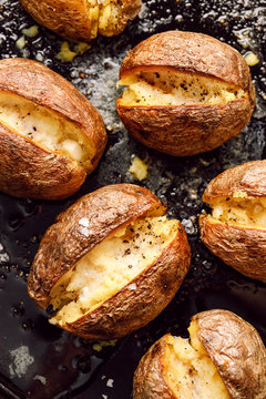 Baked potato, hot baked potatoes with the addition of butter and freshly ground black pepper and sea salt flakes on a black background, top view