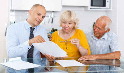 Aged couple signing financial agreement with bank worker