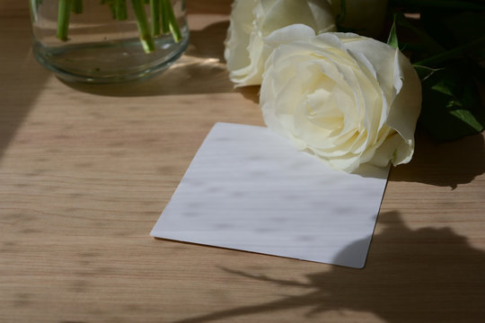 blank white paper of wedding card put on wooden table with romantic rose flower in morning day, image used for design your text greeting with love