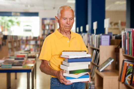 Portrait of joyous older man in library with pile of books in hands