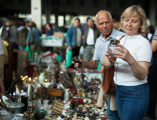 Attentive mature spouses buying retro handicrafts on flea market