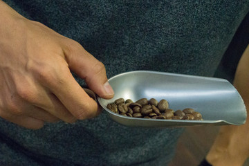 man holds a spatula with grains of coffee