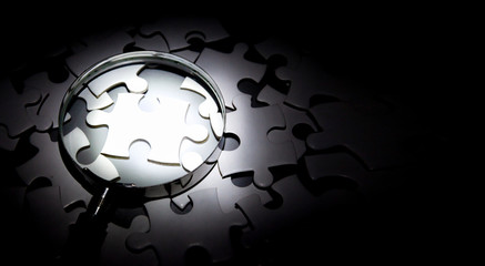 Magnifying glass In the dark with light shining to find piece of jigsaw puzzle