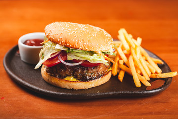 Fast food. Homemade hamburger and french fries on black plate.