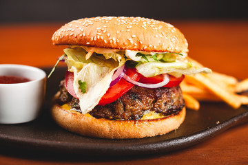 Fast food. Homemade hamburger and french fries on black plate.
