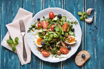 Salad of arugula, tomatoes, nuts and eggs. View from above. Wooden table. Place for text.