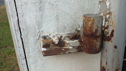 Close up of a rusted hinge with weathered metal door