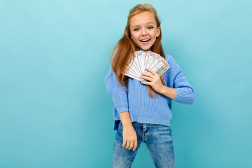 Fototapeta na wymiar Portrait of little caucasian girl with long brow hair in blue hoody holds a lot of money isolated on blue background
