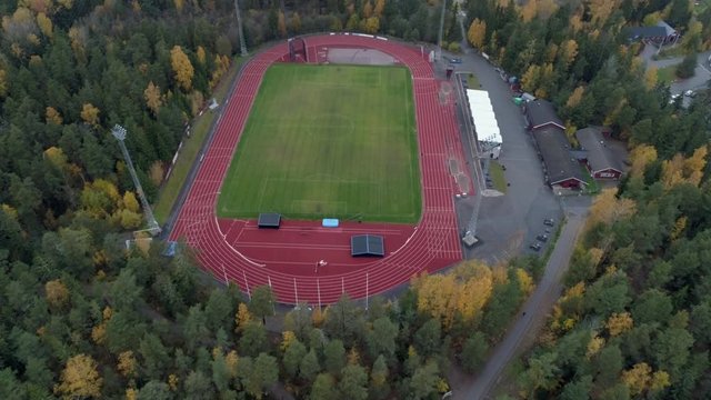 Aerial view of soccer field and running tracks in the forest. Drone shot flying over football field and athletic field in the autumn. Sports background in 4K resolution. Stockholm, Sweden