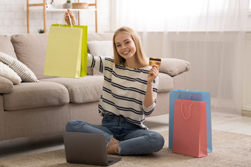 Joyful young lady holding colorful shopping bag and credit card