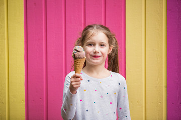 Cute little girl eating chocolate ice cream. Smiling and laughing. Colorful pink and yellow wall on background. Bright summer concept