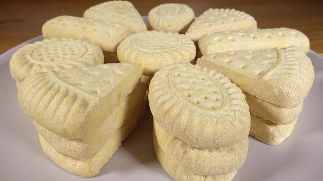 Close POV circular dolly shot of an assortment of buttery, baked, shortbread biscuits / cookies on a plate, dusted with sugar.