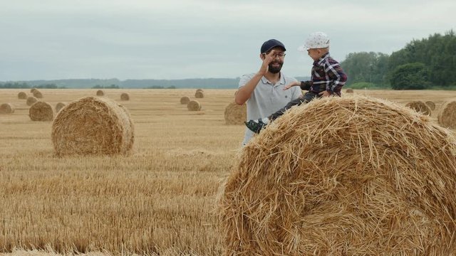 Dad plays with his little son in a field sitting on a haystack, give me five