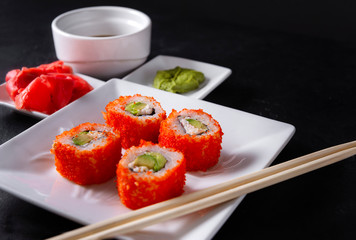 4 Japanese rolls with fish ROE on a white plate, ginger, wasabi, sticks on a black background, Japanese cuisine