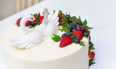 white birthday cake with 2 swans made of sugar mastic with fresh berries kolubniki and blueberries