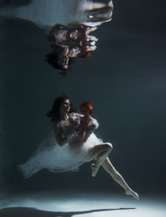 Beautiful girl swims with an underwater doll in the pool in a beautiful white dress.