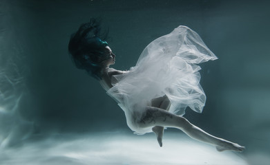A beautiful girl with blue and long hair swims underwater in the pool in a fluffy white dress....