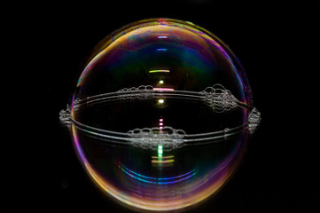Colorful soap bubble on a black mirrored surface