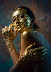 Girl with a mask on her face made of gold leaf. Gloomy studio portrait of a brunette on an abstract background.