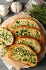 Plate with toasted garlic bread and dill on wooden background, top view