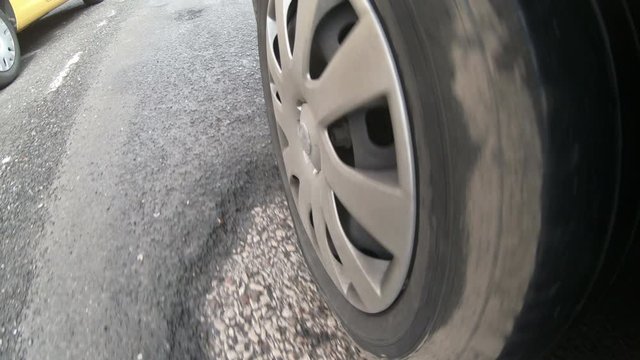 Vehicle tyre driving over a damaged road which is covered in Potholes in the street.  POV camera attached to side