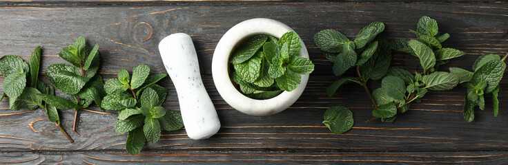 Mortar, pestle and mint on wooden background, top view