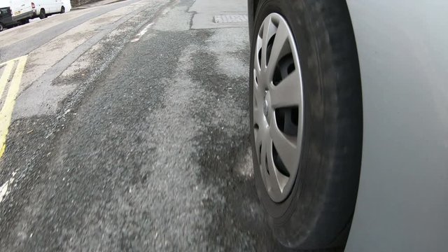 Vehicle tyre driving over a damaged street which is covered in Potholes in the road.  POV camera attached to side