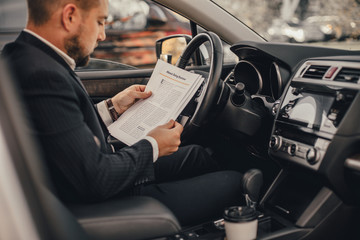 Handsome caucasian businessman driver inside in vehicle  with coffee and gadget and check mail and talking with partners