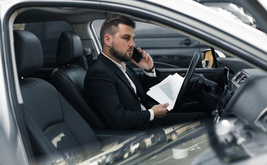 Fototapeta na wymiar Handsome caucasian businessman driver inside in vehicle with coffee and gadget and check mail and talking with partners