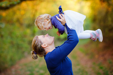 Happy young mother having fun cute toddler daughter, family portrait together. Woman with beautiful baby girl in nature and forest. Mum with little child outdoors, hugging. Love, bonding.