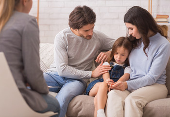 Worried parents comforting their little daughter at psychologist consultation