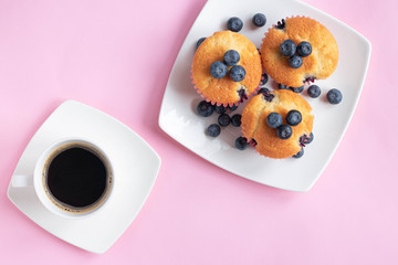  Blueberry cupcakes and cup of coffee on pink background. Perfect breakfast and start of the day. Top view
