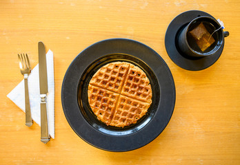 Overhead view of a waffle breakfast with tea and utensils.